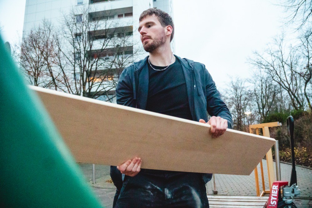 Ein Mitarbeiter von Erben & Räumen trägt eine große Holzplatte zum Container vor einem Wohnhaus