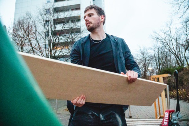 Ein Mitarbeiter trägt eine große Holzplatte zum Container