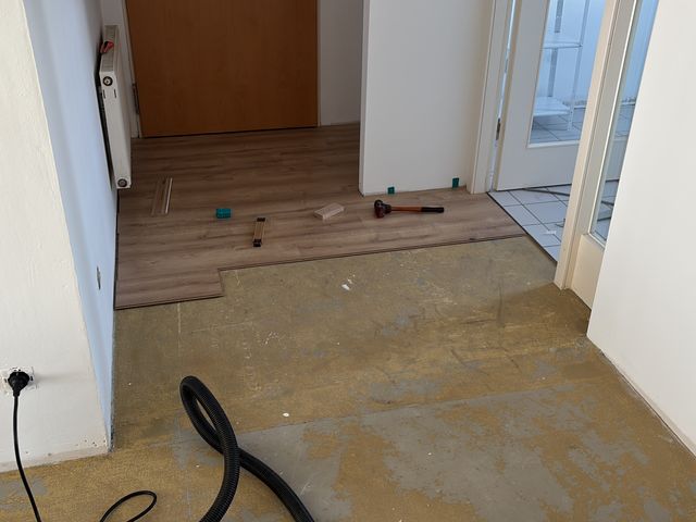 Flur mit freigelegtem Untergrund, die ersten Dielen in Holzoptik liegen, daneben Werkzeug