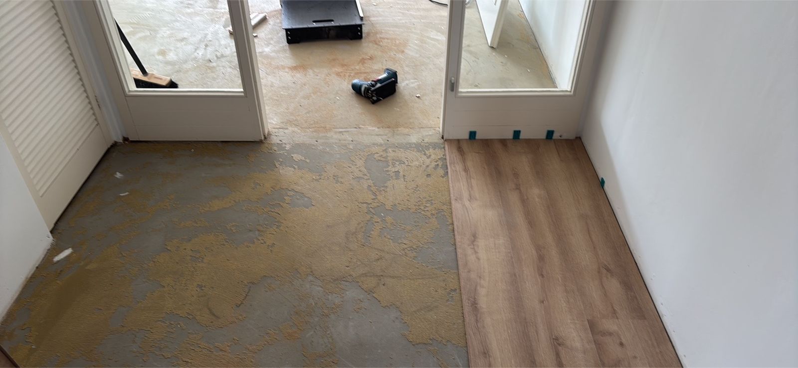 Flur mit zwei Glastüren: links der freigelegte Untergrund mit alten Kleberresten, rechts der neu verlegte Boden in Holzoptik