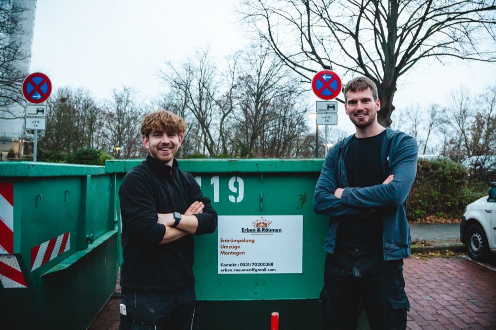 Zwei Mitarbeiter von Erben & Räumen stehen vor einem grünen Absetzcontainer mit Firmenschild