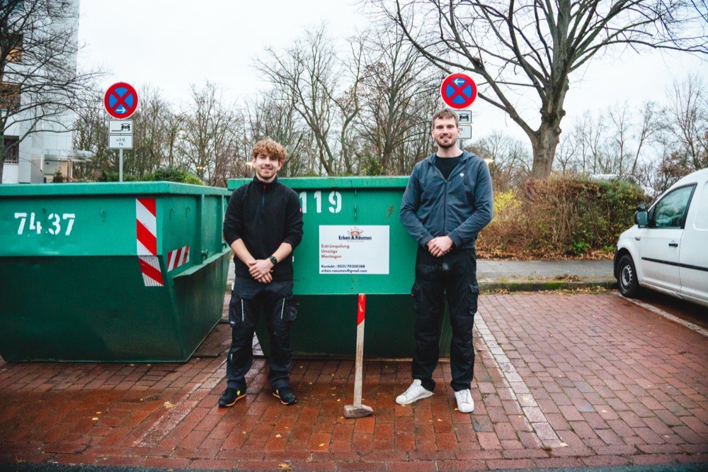 Zwei Mitarbeiter von Erben & Räumen stehen vor zwei grünen Absetzcontainern mit Firmenschild