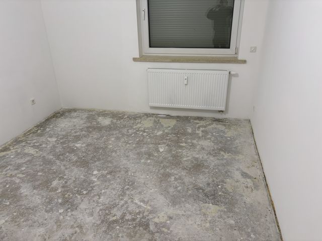 Leeres Zimmer mit weißen Wänden, der alte Bodenbelag ist entfernt