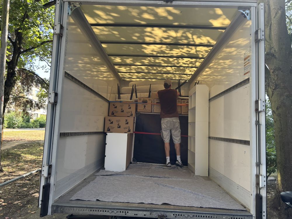 Ein Mitarbeiter belädt einen Umzugswagen, Kartons und Möbel sind mit Gurten gesichert, der Boden ist mit Decken ausgelegt